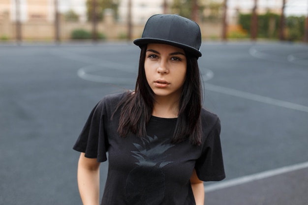 Photo stylish beautiful young urban hipster woman with black baseball cap mockup in black tshirt on the street