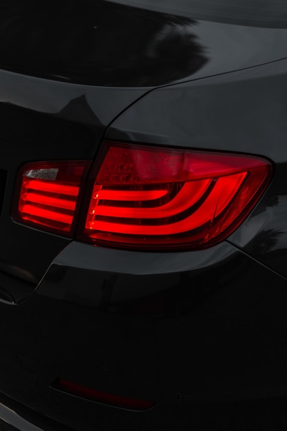 Stylish black metal car with a red brake light on a dark background Beautiful transport wallpaper