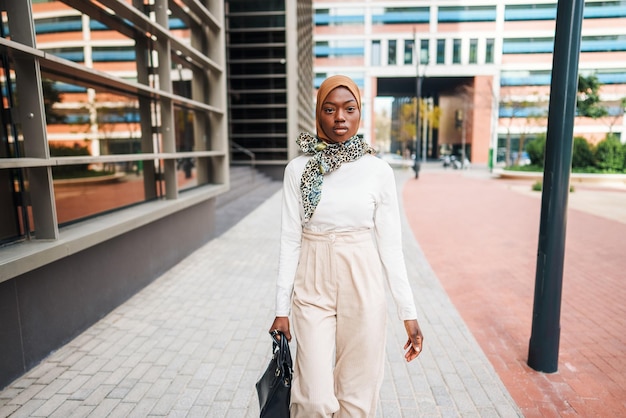 Stylish black muslim woman with bag observing high buildings