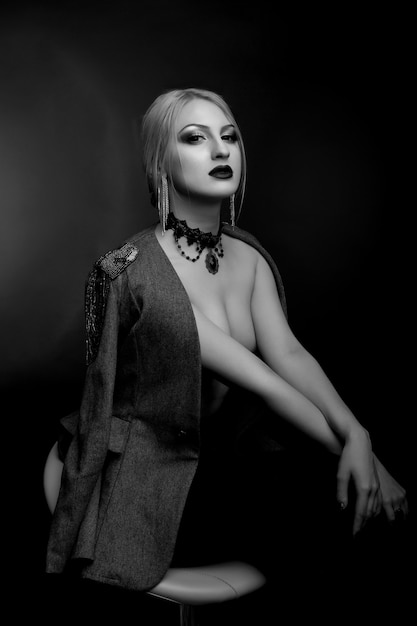 Stylish black and white studio portrait of a amazing woman with bright makeup wears jacket on a naked body