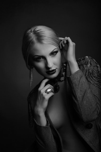 Stylish black and white studio portrait of a magnificent lady with bright makeup wears jacket on a naked body