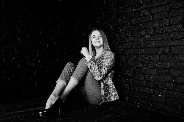 Stylish blonde girl in jacket and jeans against brick black wall .