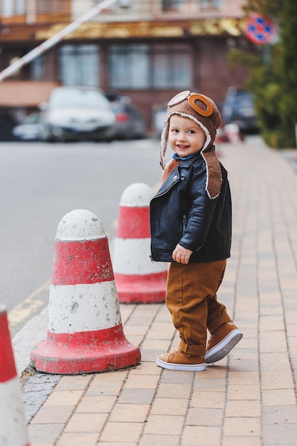 Stylish boy 3 years old in a leather jacket and brown trousers walks on the street Modern child Children's fashion Happy child