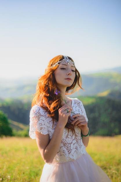 Stylish bride standing on beautiful landscape of mountains on sunset