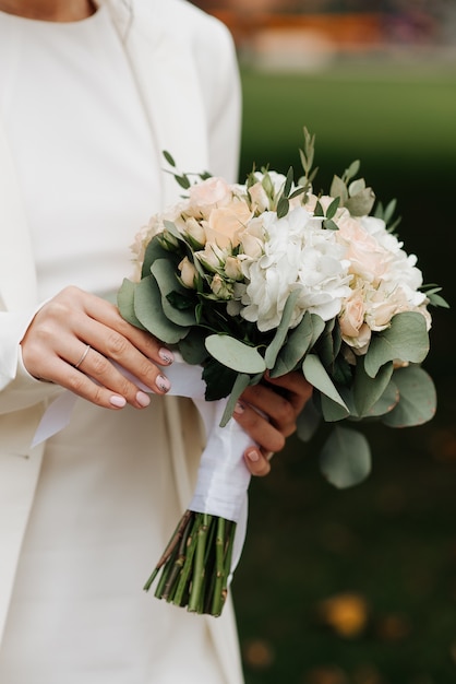 Stylish bride in a white dress and manicure holding a wedding bouquet