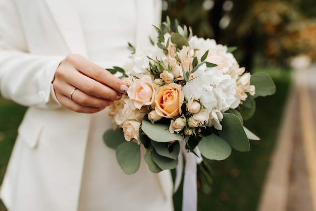 Stylish bride in a white dress and manicure holding a wedding bouquet