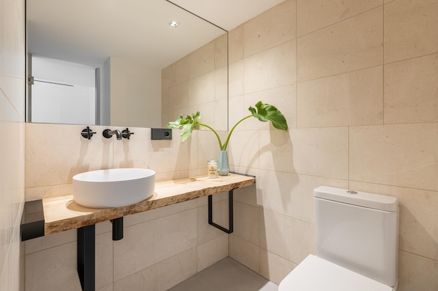 Stylish bright bathroom with beige tiles on the walls and a large mirror with a sink in a wooden