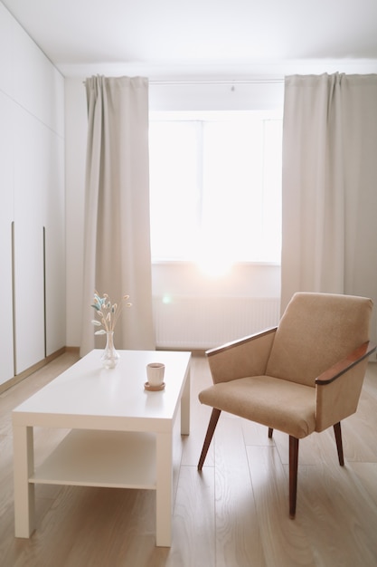 Stylish bright living room with comfortable armchair and table by the window.