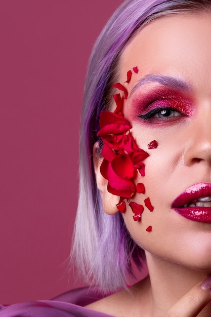 Stylish and bright young woman with colored makeup and flower petals on her face