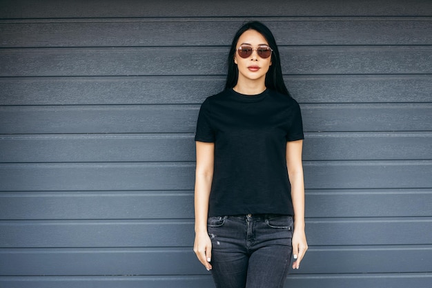 Stylish brunette asian girl wearing black tshirt and sunglasses posing against street urban cloth