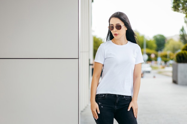 Stylish brunette asian girl wearing white tshirt and sunglasses posing against street urban cloth