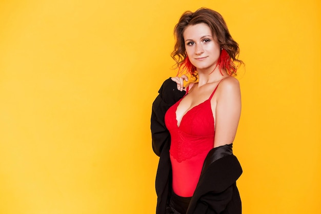 Stylish brunette girl posing on an orange background in a sexy red top and a black jacket with ostrich feather earrings