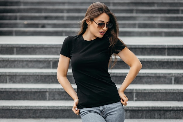 Stylish brunette girl wearing black tshirt and glasses posing against street  urban clothing style