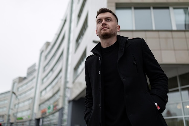 Stylish brutal man in a black coat on the background of city buildings