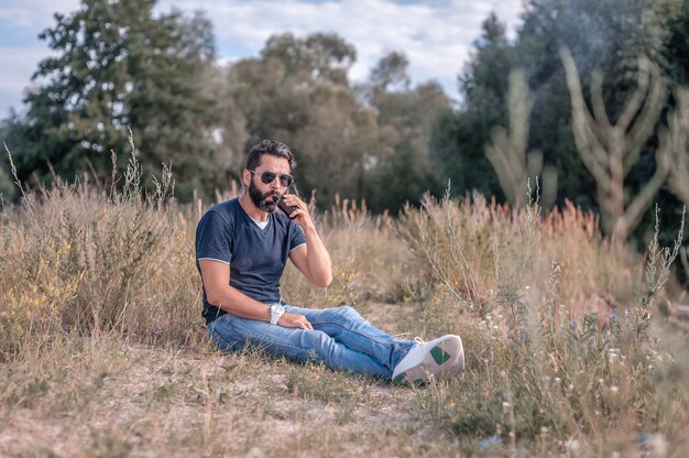 Stylish brutal man smoking an vape on the forest floor