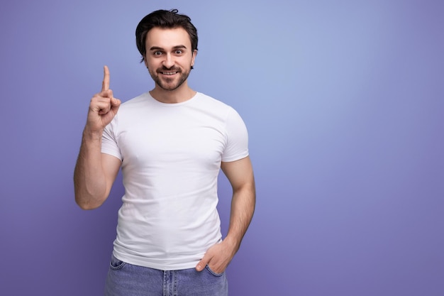 Stylish brutal strong brunette man in a white tshirt with muscles points a finger to the side