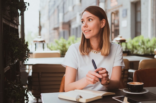 Stylish business woman in a street cafe making notes in a notebook and drinks coffee