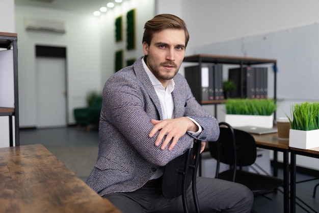 Stylish businessman in formal suit sitting seriously looking at camera in office