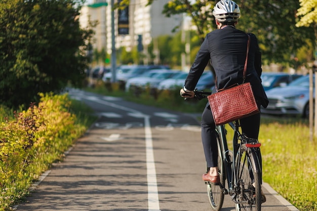 Stylish businessman in helmet cycling on bike path in sunny day