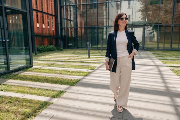 Photo a stylish businesswoman confidently walks outdoors in a modern office complex during the day