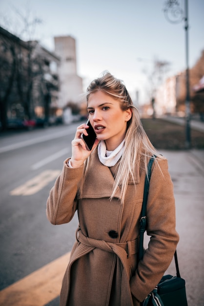 Stylish businesswoman using smart phone while waiting for a taxi.