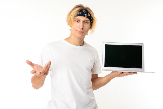 Stylish caucasian blonde man shows and recommend laptop isolated on white wall