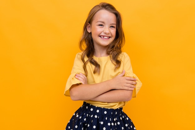 Stylish charming young smiling girl in a light yellow blouse and skirt on a yellow wall