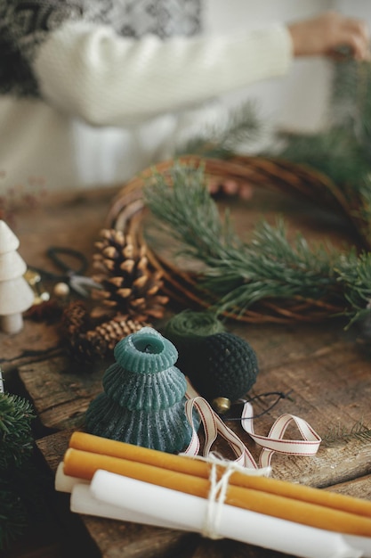 Stylish christmas candle on background of woman in cozy sweater making christmas wreath Advent