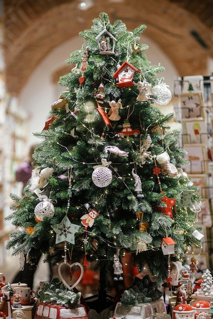 Stylish christmas tree with ornaments and toys in store showcase in evening Modern christmas decor in city street Atmospheric winter holidays in Europe Merry Christmas and Happy Holidays