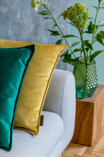 Stylish composition of cozy living room with sofa, wooden cube, nice interior details and neutral classy pillows. Green and grey creative wall and parquet floor. Scandinavian style.