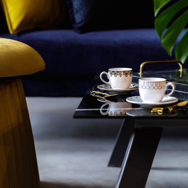 Stylish composition at living room interior with gold pouf velvet sofa pillows coffee table tropical leaf and cups of coffee in modern concept