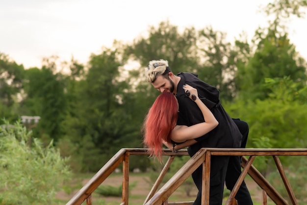 Stylish couple in love in black clothes are walking in the park and hugging Lovely hipster couple smiling and enjoying time together Youth love and lifestyle concept