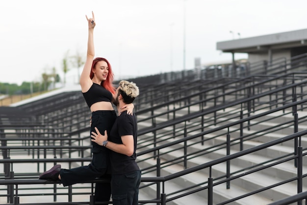 Stylish couple in love in black clothes walks in the park and hugs Lovely couple of hipsters hugging on the background of the stairs Emotional girl with hands up