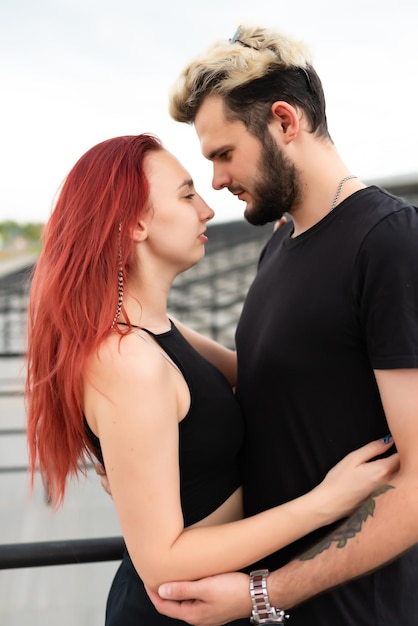 Stylish couple in love in black clothes walks in the park and hugs Lovely couple of hipsters hugging on the background of the stairs Youth love and lifestyle concept