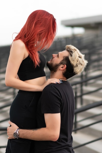 Stylish couple in love in black clothes walks in the park and hugs Lovely couple of hipsters hugging on the background of the stairs Youth love and lifestyle concept