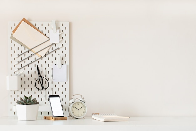 Stylish desk interior with White table background with plant and leaves. Modern home office interior