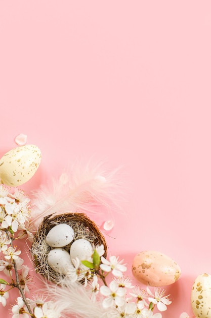 Stylish Easter eggs in nest cherry blossoms and feathers flat lay on pink background with copy space Happy Easter Greeting card template Modern spring holiday banner