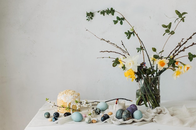 Photo stylish easter eggs panettone and spring flowers on linen cloth on rustic table natural dye eggs and daffodils bouquet festive minimal still life happy easter