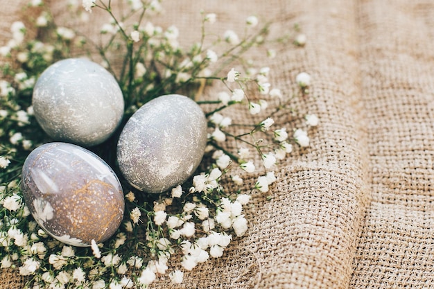 Photo stylish easter eggs with spring flowers in floral nest on rustic fabric in sunny light on wood modern colorful eggs painted with natural dye in grey marble happy easter greeting card