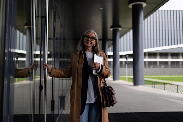 Stylish elderly business woman enters the mall with a laptop in her hands