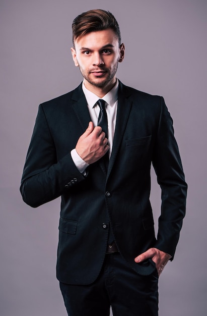 Stylish elegant and confident young business man is possing on grey background