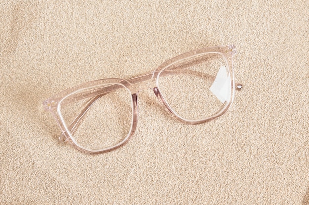 Stylish eye glasses in a transparent plastic frame on the sand top view copy space