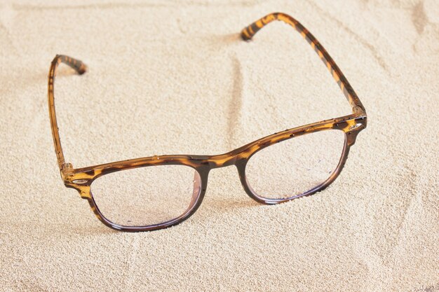 Stylish eye glasses with spotted plastic frames on the sand, copy space top view