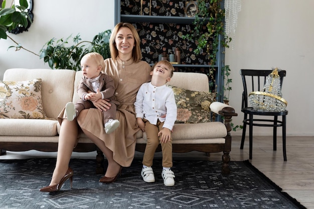 Stylish family mom and two little sons are sitting on the sofa and watching the camera