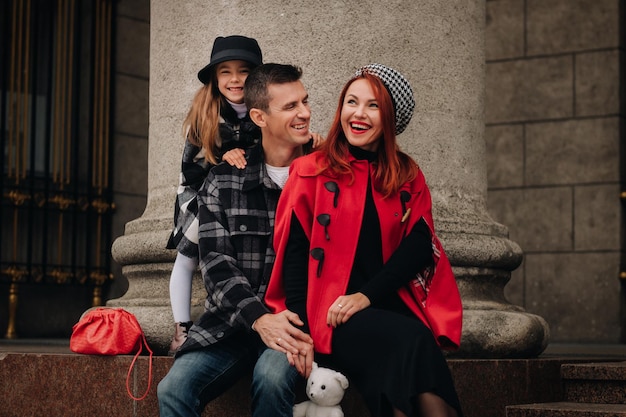 A stylish family of three strolls through the autumn city posing for a photographer Dad mom and daughter in the autumn city