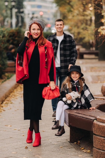 A stylish family of three strolls through the autumn city posing for a photographer Dad mom and daughter in the autumn city