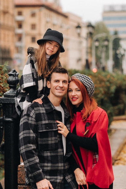 A stylish family of three strolls through the autumn city posing for a photographer Dad mom and daughter in the autumn city