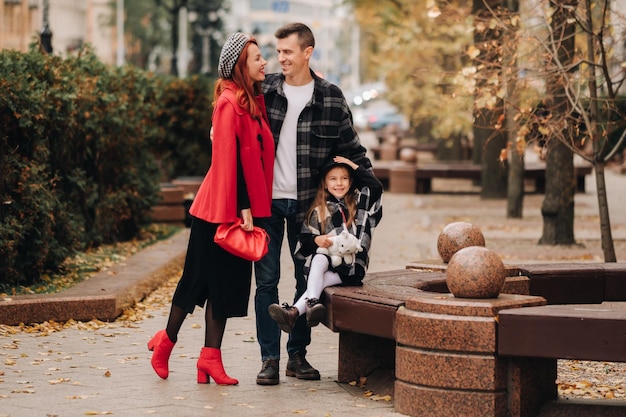 A stylish family of three strolls through the autumn city posing for a photographer Dad mom and daughter in the autumn city