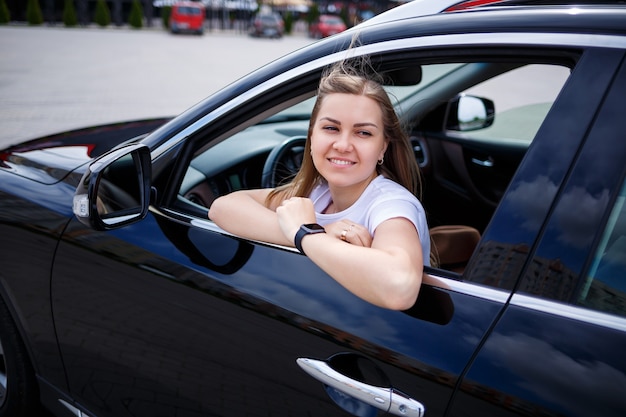 Stylish fashionable beautiful girl sitting in the salon of a black business class car. Young woman with a smile on her face. Woman in a car park