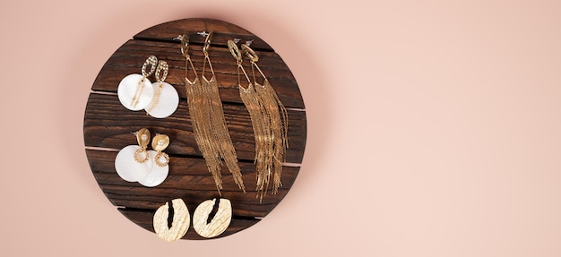 Stylish female jewelry on dark wooden stand on pink background Fashion and style concept Top view of golden earrings